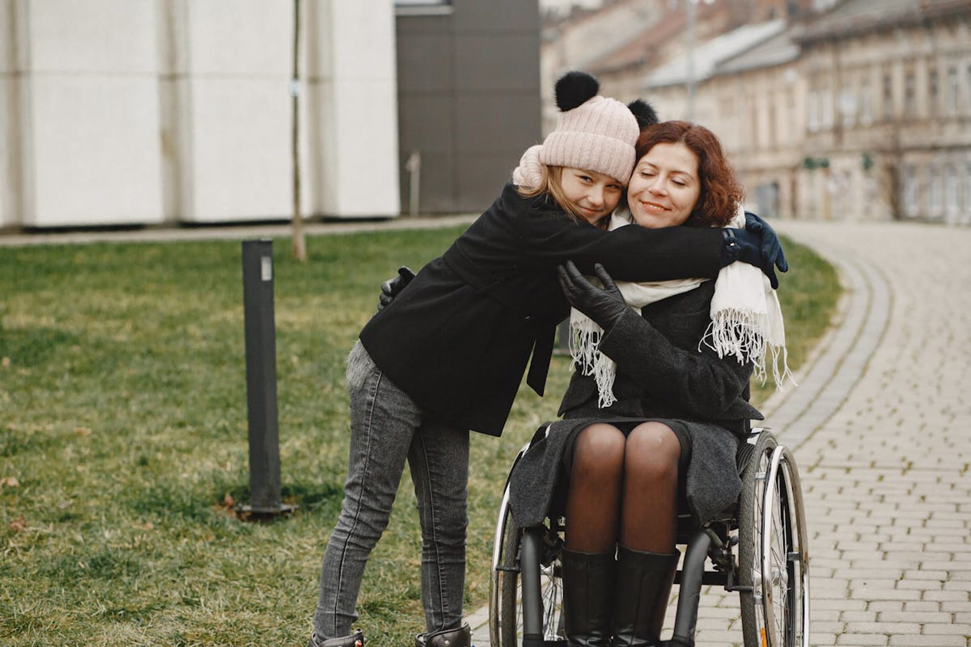 Child hugging woman in a wheelchair outdoors, both smiling