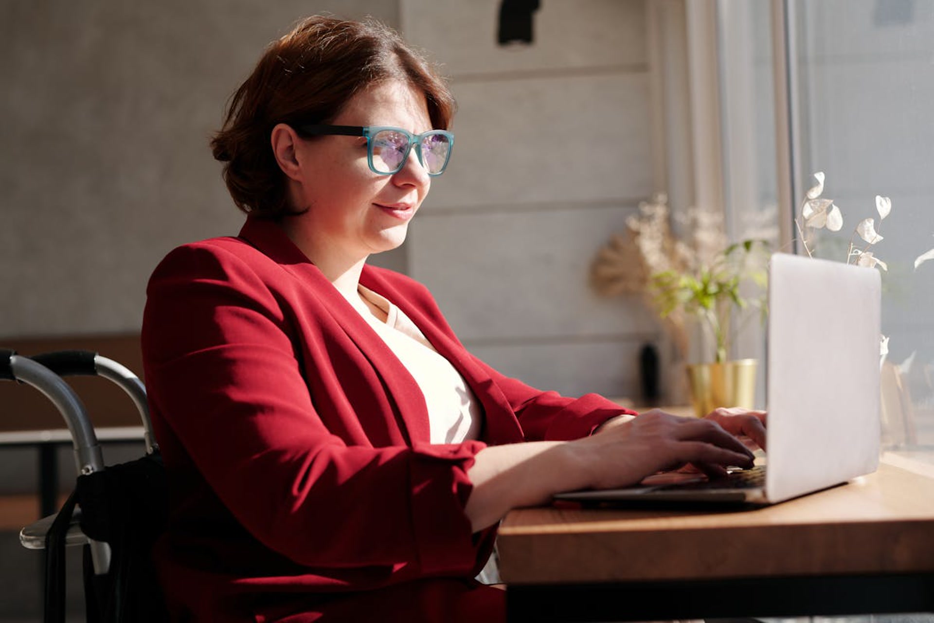 Woman in wheelchair wearing a red blazer in a café setting, confident and professional