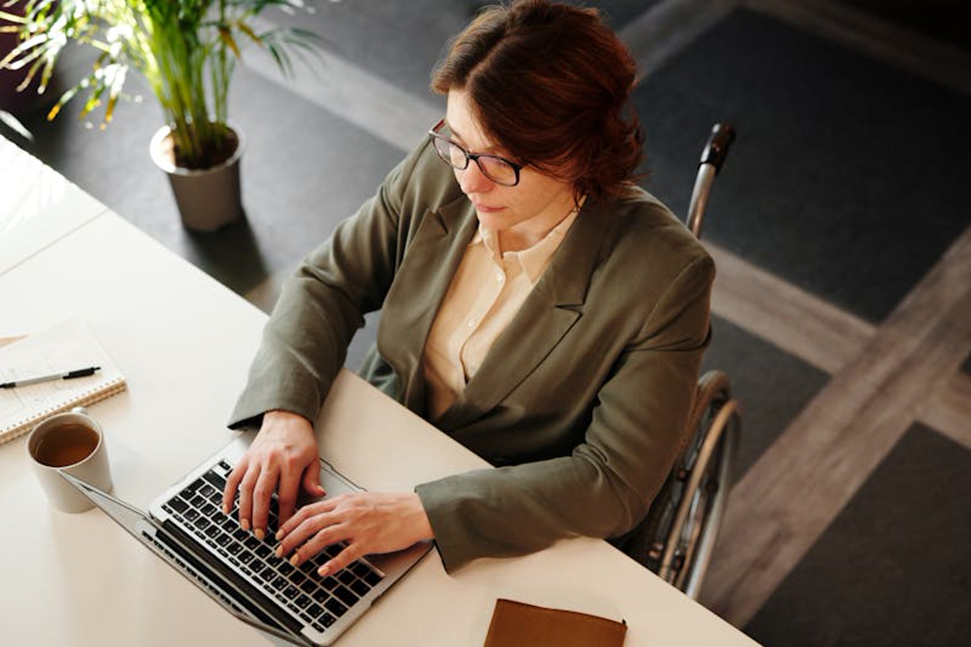Professional woman in a wheelchair typing on a laptop in a modern office, showcasing skilled employment support